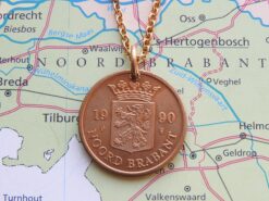 Koperen Noord-Brabant rijkspenning uit 1990 aan goudkleurige kettinkje, met leeuwwapen en opschrift op kaartachtergrond.