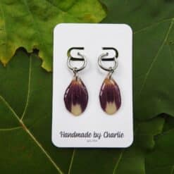Paarse en witte dahlia-oorringen in druppelvorm aan zilveren ringen, op een witte kaart met "Handmade by Charlie" tekst.