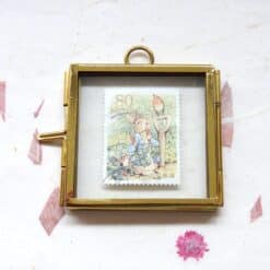 Goudkleurig vierkant lijstje met een vintage Japanse postzegel van Pieter Konijn met tuinkabouter onder glas, voorzien van een oogje.
