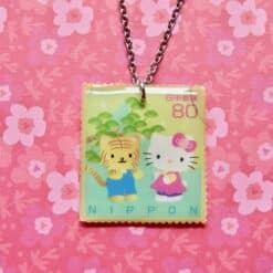 Hello Kitty postzegelketting met Japanse postzegel design, zilveren ketting en vierkant hanger met Hello Kitty en kat illustratie.