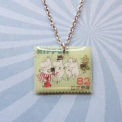 Moomin postzegelhanger met geel postzegelontwerp en karakters aan zilveren ketting.