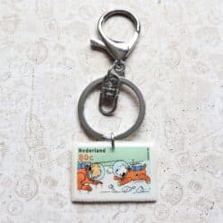 Zilveren sleutelhanger met Nederlandse postzegel van Kuifje, 80 cent waarde, met kleurrijke afbeelding van het stripfiguur.