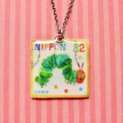 Rupsje Nooitgenoeg postzegelketting met gele rand, groene rups en rode appel aan zilveren ketting.